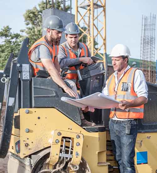 NYC construction workers reviewing blueprints on site with heavy equipment